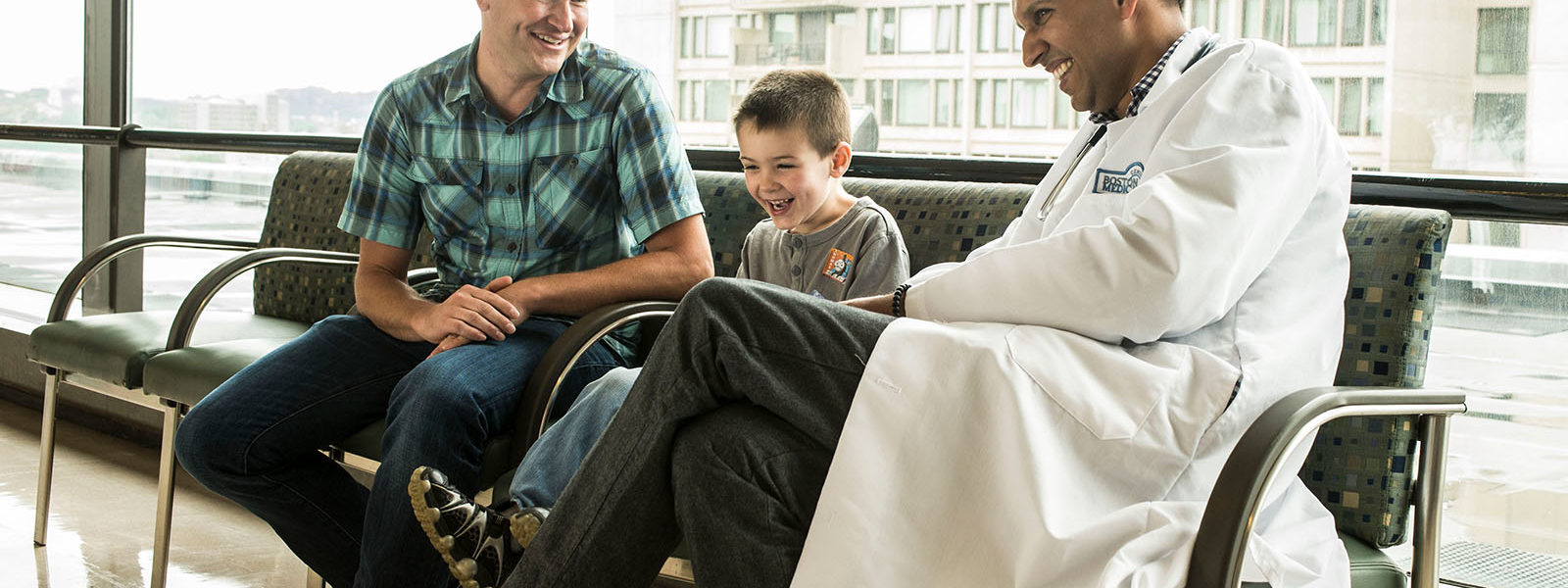 father with son laughing and sitting with physician in hospital lobby