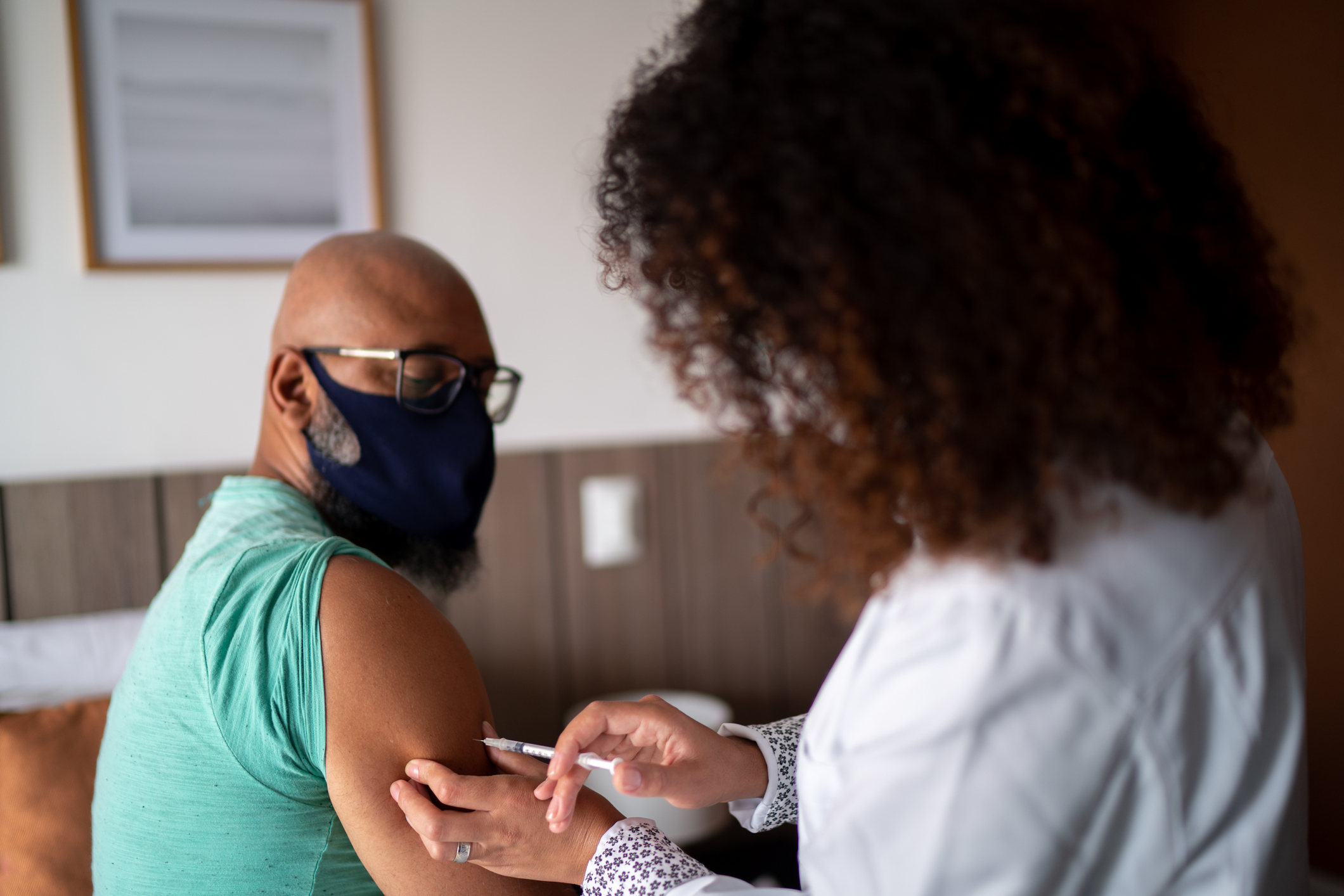 Home call nurse or doctor vaccinating a man at home – wearing face mask